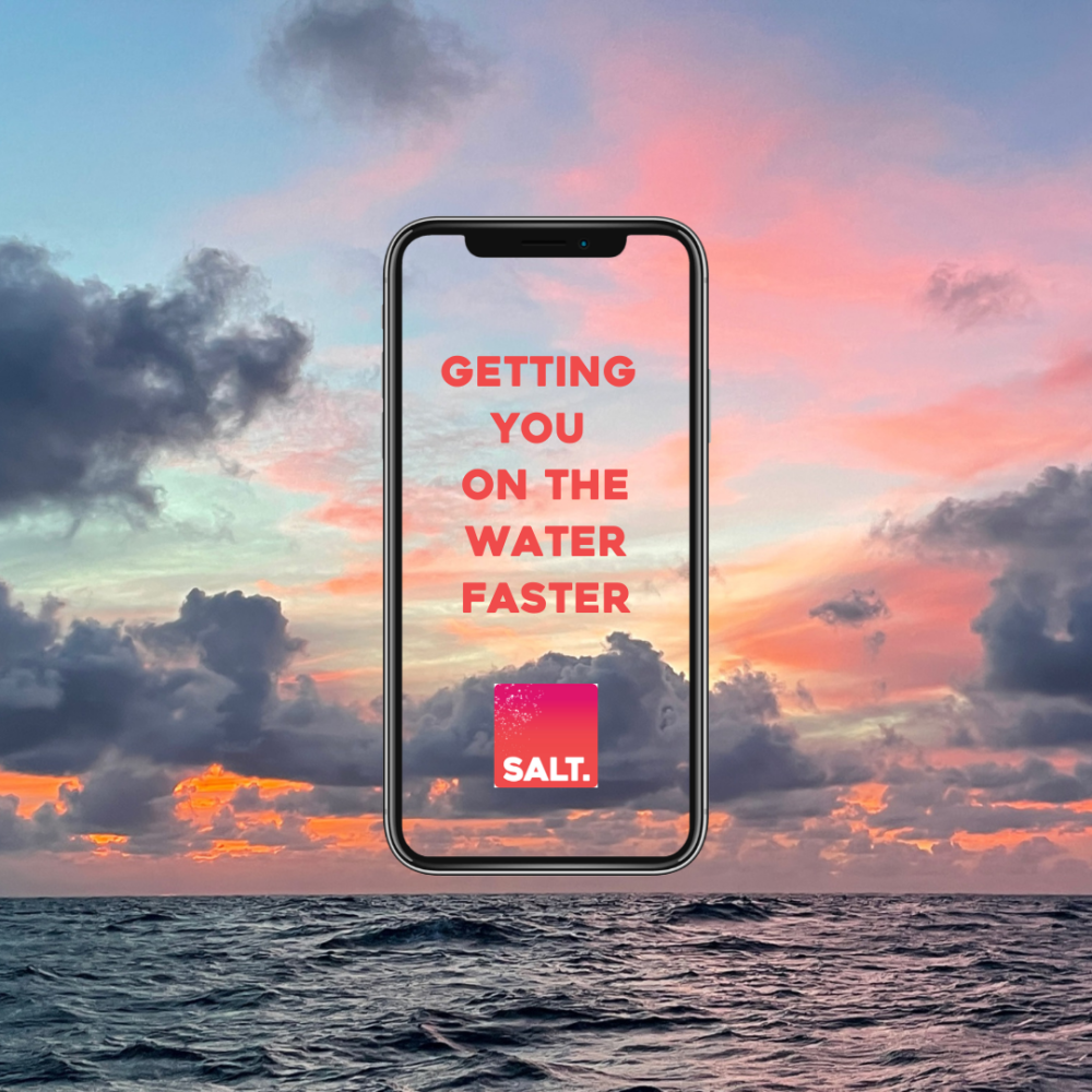 A phone showing the SALT app slogan “Getting you on the water faster”, against a sunset sky over the sea