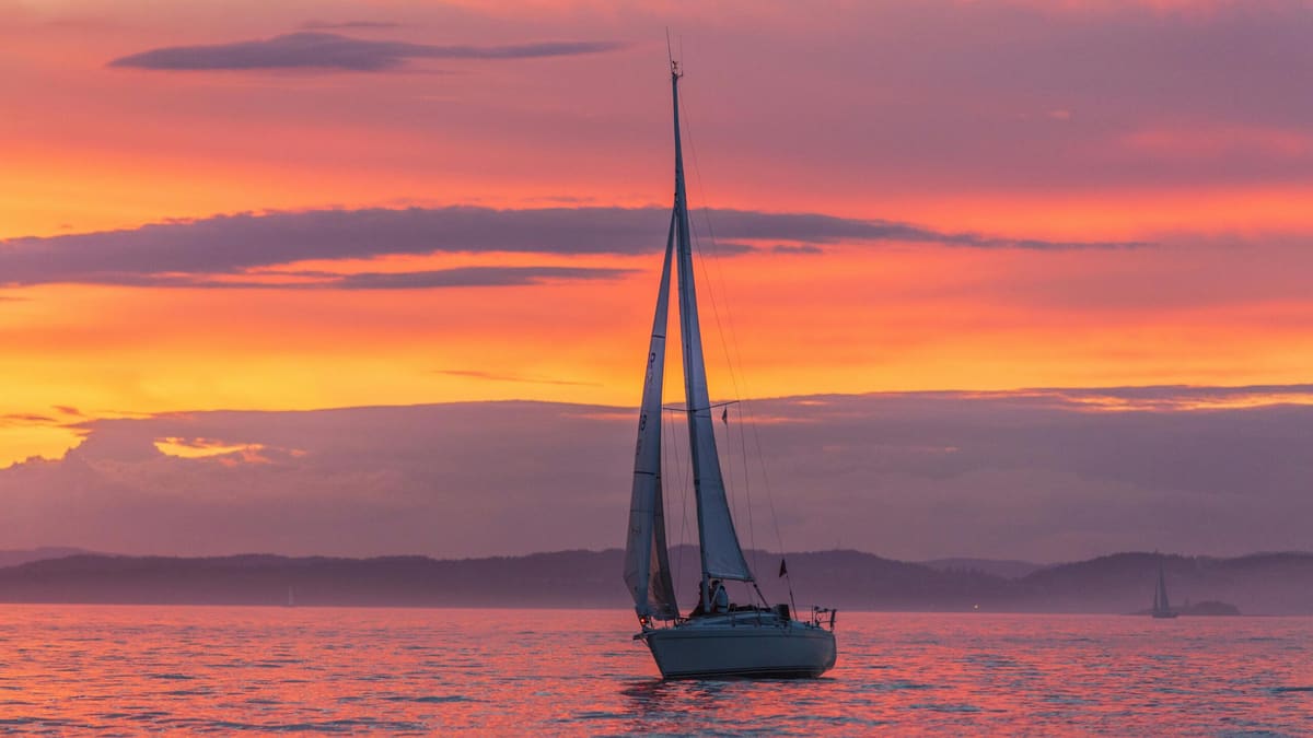 A sailing yacht drifting under a pink and orange sunset